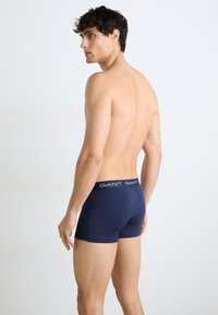 Blå bomulls boxershorts med en tettsittende design og en logo midje, båret av en modell sett fra baksiden, mot en ensfarget bakgrunn.