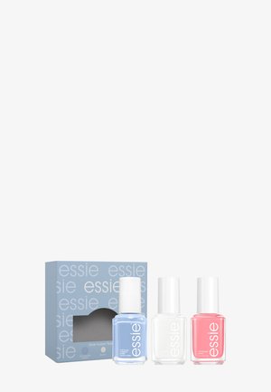 Trois flacons de vernis à ongles bleu, blanc et rose avec une boîte bleue étiquetée « essie » derrière.