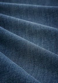 Tmavě modrá denimová tkanina s viditelnou texturou keprového tkaní, s jemnými světlými vzory a hladkým, mírně elastickým povrchem.