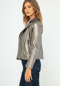 Veste de moto en faux cuir argent métallisé avec un motif matelassé sur les manches, poches zippées et un design de col cranté.