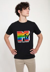 Černé bavlněné tričko s barevným duhovým pruhovaným logem MTV, pod kterým je bíly text "MUSIC TELEVISION" a volný střih.