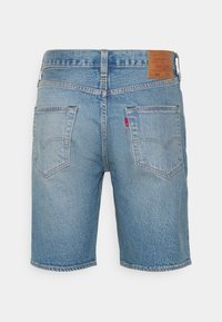 Vue arrière d'un short en denim bleu mi-long avec deux poches arrière, passants de ceinture, une étiquette en cuir et une petite étiquette en tissu rouge.