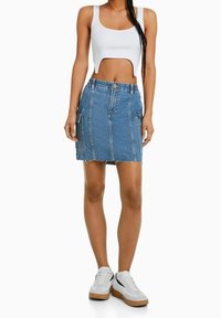 Džínová sukně ve světle modré barvě s roztrhaným lemem a čtyřmi kapsami. V kombinaci s bílým úzkým crop topem a bílými teniskami s gumovou podrážkou.