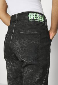 Pantalones de mezclilla negros con un acabado desgastado, que cuentan con el logo verde de Diesel en la cinturilla. Costuras visibles y dos bolsillos traseros.