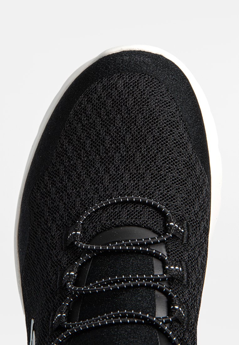Zapatilla deportiva negra con parte superior de malla texturizada, con cordones negros y suela blanca. Diseño minimalista con forma aerodinámica y acentos.