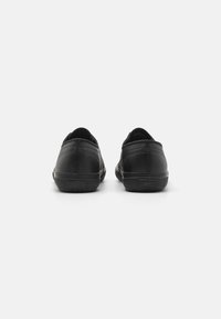 Black leather shoes with a smooth texture, low profile, and rounded back. Features a rubber sole and subtle stitching detail.