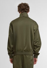 Maslinasto zelena bomber jakna od poliestera s visokim ovratnikom, rebrastim manžetama i rubom; ima glatku teksturu i opušten kroj.