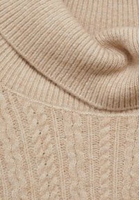 Pull en maille beige clair avec une texture côtelée et un motif de torsades. Tissu doux avec un col retourné.