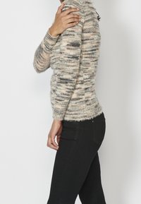 Stickad tröja i ljusbeige med mörka prickar, med hög krage och långa ärmar. Bärs med figurnära svarta byxor. Mjuk, texturerad tyg.