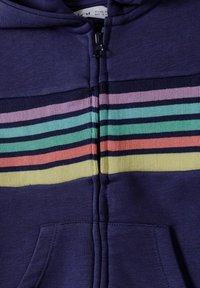 Navy vetoketjuhuppari, jossa on vaakasuorat raidat pasteliväreissä: violetti, vihreä, oranssi ja keltainen, ribbikuviointi ja sivutaskut.