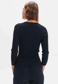 Maglione nero a coste con maniche lunghe e silhouette aderente. Presenta un collo rotondo e un tessuto testurizzato, visto da dietro.
