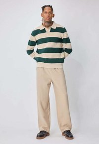 Polo en maille à rayures vertes et beiges, coupe décontractée, associé à un pantalon beige à jambes larges et des chaussures en cuir noir avec semelles marron.