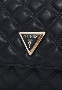 Black quilted synthetic leather handbag featuring a gold-tone triangular logo plate with "GUESS" and "U.S.A." in contrasting black.