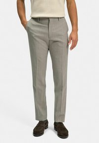 Ljusgrå skräddarsydda byxor med subtil textur, rak front och sidfickor. I kombination med mörkbruna loafers, mot en neutral bakgrund.