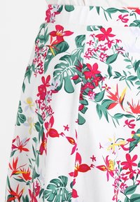 Falda floral con fondo blanco, flores rojas, rosas y amarillas vibrantes, y hojas verdes. El material parece ligero con una cintura fruncida.