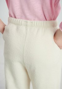 Pantalon en polaire de couleur crème avec une surface texturée et une taille élastique, doté de poches latérales et d'une coupe décontractée.