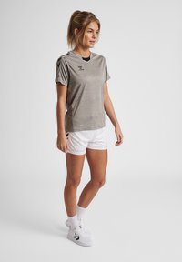 Grå atletisk t-shirt med korte ærmer, med en sort halsudskæring og logo. Sammen med hvide shorts og sporty fodtøj.