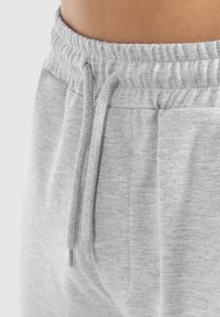 Pantalons de survêtement en coton gris avec une taille élastique côtelée, un cordon de serrage réglable et des poches latérales, le tout dans une texture douce.