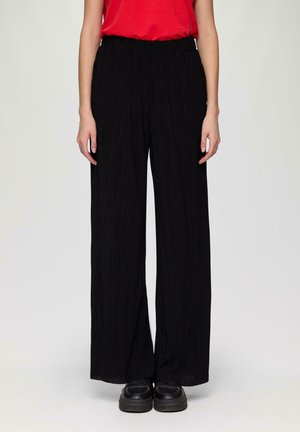 Black pleated wide-leg pants with an elastic waistband, made from lightweight fabric, paired with black chunky shoes.