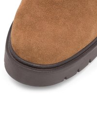 Hnedá semišová obuv s okrúhlou špičkou, kontrastnou tmavou gumovou podrážkou a jemnými detailmi šitia pozdĺž okraja.