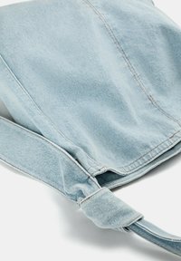 Svetlomodrá denim taška s jemnou textúrou, vybavená viazaným popruhom a viditeľnými švovými detailmi. Štruktúrovaný dizajn s neformálnym vzhľadom.