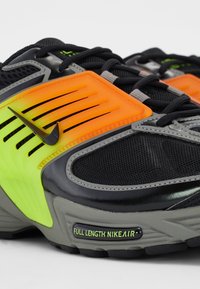 Černé sportovní boty mají síťované panely a jasné oranžové a zelené akcenty. Design zahrnuje strukturované vrstvy a branding "FULL LENGTH NIKEAIR".