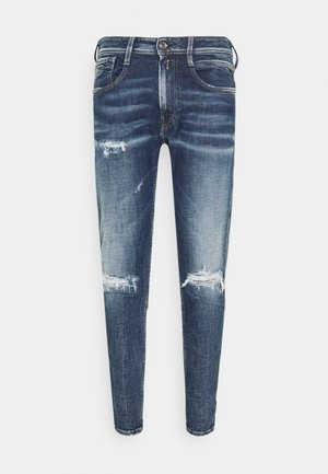 Jean slim bleu avec lavage délavé et déchirures usées sur les cuisses et les genoux, style cinq poches avec fermeture avant par bouton et fermeture éclair.