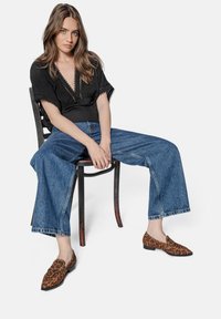 Black short-sleeve blouse with lace trim, high-waisted wide-leg blue denim jeans, and brown leopard print slip-on shoes.