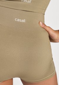 Μπεζ αθλητικές βερμούδες με ριγέ υφή, διαθέτοντας φαρδιά ελαστική μέση και ένα μικρό λευκό λογότυπο που αναγράφει "casall."