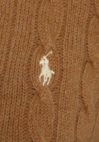 Brunt stickad tyg med en krämfärgad broderad logotyp av en polospelare på en häst som håller i en klubba.