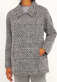 Šedý a černý kostkovaný kabát s velkým límcem, dvěma předními kapsami a texturovanou látkou. Design se vyznačuje volně střiženou siluetou.