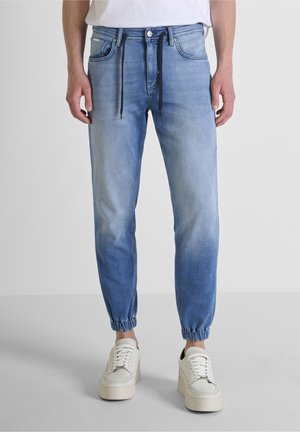 Mann trägt hellblaue Jogger-Jeans mit elastischen Bündchen und schwarzen Kordeln, kombiniert mit weißen Plateau-Sneakers.