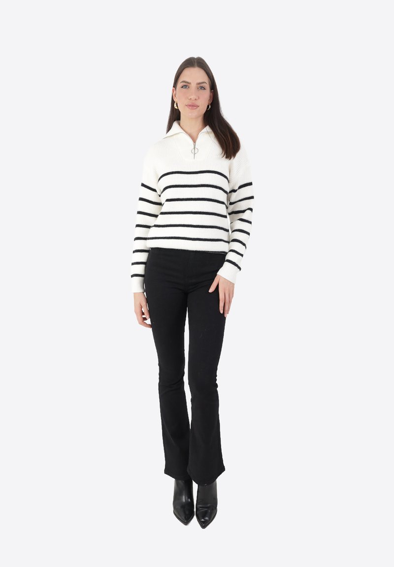 Maglione a righe crema e nero con colletto con zip, abbinato a pantaloni neri a palazzo aderenti e décolleté nere a punta. Texture a maglia liscia.