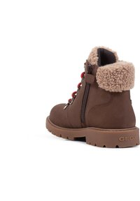 Botín de ante marrón que cuenta con un cuello de piel sintética, cordones rojos y un zipper lateral. La suela tiene una textura con un patrón de agarre resistente. Se puede ver la marca GEOX.