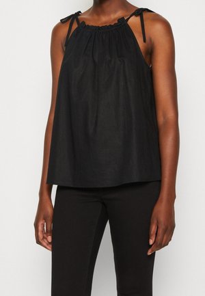 Haut noir sans manches style tour de cou avec encolure froncée et bretelles nouées aux épaules, porté avec un pantalon noir sur une personne à la peau foncée.