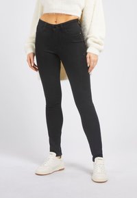 Černé skinny džíny vyrobené z denimu, s klasickým 5-kapsovým designem a vysokým pasem. V kombinaci s bílými teniskami pro kontrast.