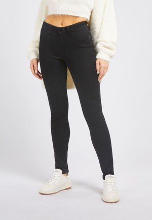 Jean skinny noir en denim, avec un design classique à 5 poches et une taille haute. Associé à des baskets blanches pour le contraste.