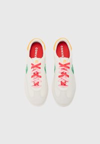 Bílé textilní tenisky s zelenými akcenty, růžovými tkaničkami a žlutým detailem na patě. Červené stélky s nápisem "CONVERSE ALL" vytištěným bílou barvou.