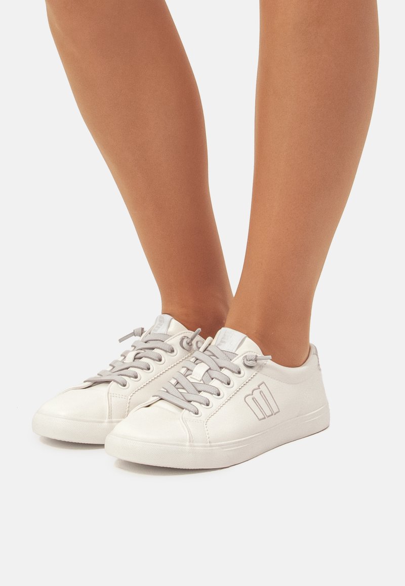 Zapatillas blancas con cordones grises, punta redonda y acabado en cuero texturizado. Presentan un logo sutil en el lado y suela de goma plana.