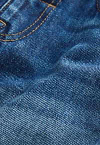 Jeans tkanina v temno modri barvi z rahlo zbledelo teksturo. Značilne so rumene šive ob šivih z rahlimi barvnimi razlikami.