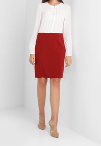 Rode jurk met een geplooide witte bovenkant, aangesloten ontwerp, knielengte en lange mouwen. Bevat een sleutelgatdetail bij de halslijn.