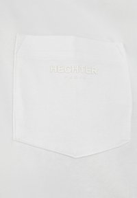 Witte katoenen t-shirt met een vierkant borstzakje waarin het geborduurde woord "HECHTER" en "PARIS" in bijpassende kleur staat. Glad van textuur.