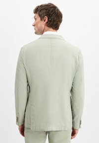 Hellgrüner Blazer aus strukturiertem Stoff, mit einem Schlitz hinten, zwei Seitentaschen und knopfbaren Manschetten.