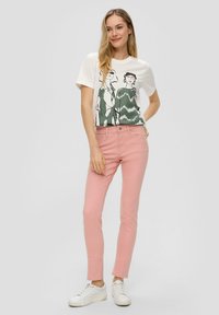 Camiseta gráfica blanca con ilustraciones verdes, combinada con unos pantalones skinny rosa claro y zapatillas blancas. Tejido suave y diseño ajustado.