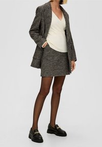 Blazer marron et noir à motif pied-de-poule sur mesure avec jupe assortie, haut crème et mocassins noirs ornés d'une chaîne dorée. Textures lisses visibles.