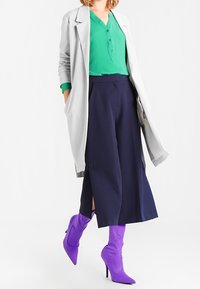 Harmaa pitkä takki vihreän yläosan päällä, tumman siniset leveälahkeiset housut ja violetit korkokengät. Ominaisuuksiin kuuluu nappi yläosassa ja halkiot housuissa.