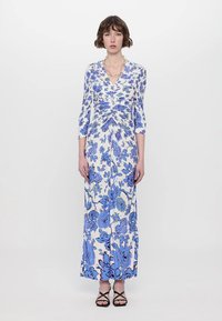 Long floral dress in white with blue flowers, featuring three-quarter sleeves and a gathered waist design. Smooth fabric, floor-length.