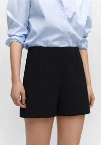 Czarne, dopasowane szorty z wysokim stanem, charakteryzujące się gładką fakturą i czystymi liniami. Połączone z jasnoniebieską koszulą na guziki.