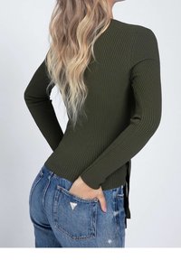 Top à manches longues côtelé vert foncé avec une coupe ajustée et un ourlet droit, associé à un jean bleu taille haute avec des fentes latérales.