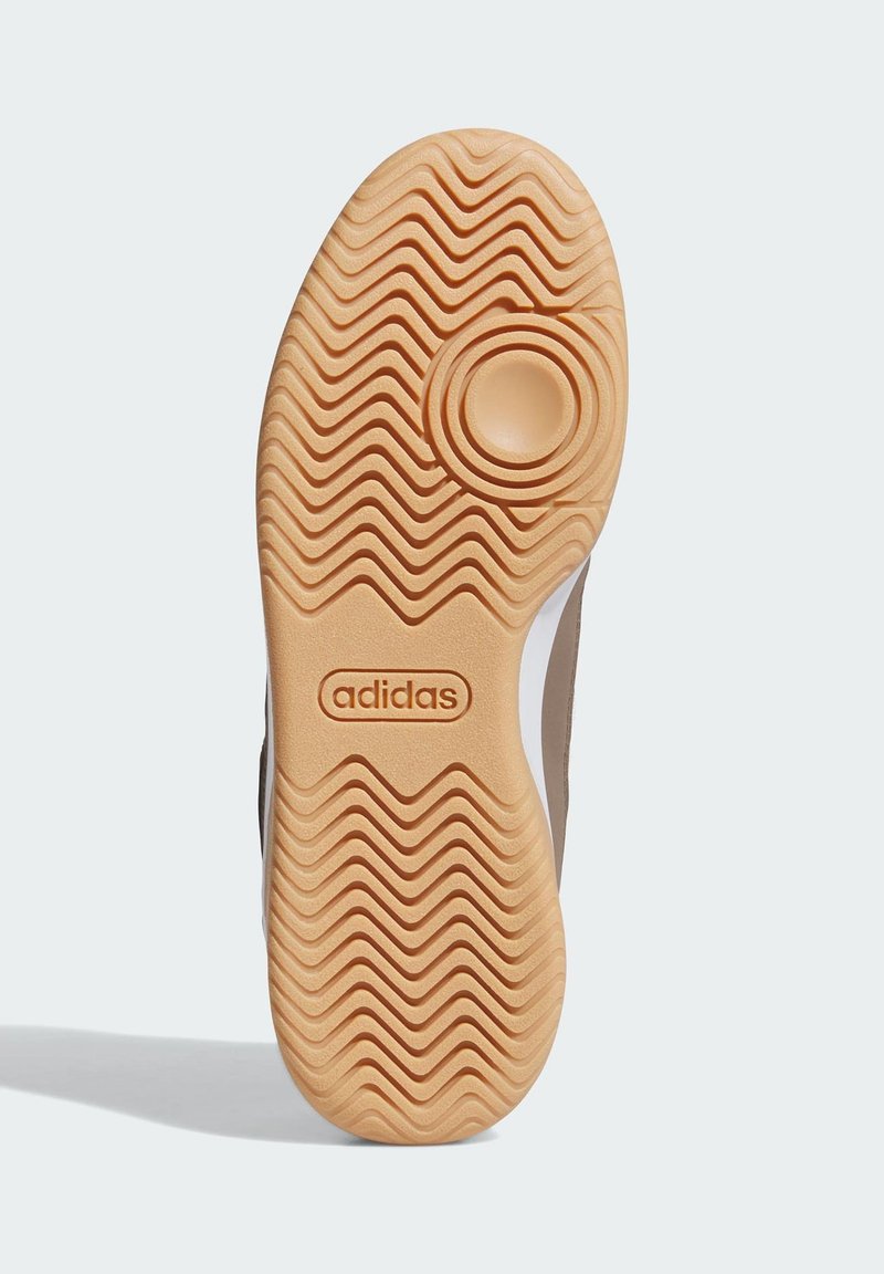 Sneaker sole with a textured, wavy pattern in tan rubber. Features a circular cutout and an engraved logo near the heel.